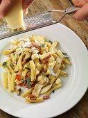 Cheese being grated over pasta with bacon and bananas