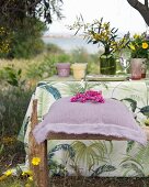 Purple linen cushion on rustic wooden bench next to set garden table