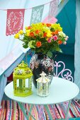Bemalte Laternen und bunter Sommerstrauss in Vase auf Gartentisch
