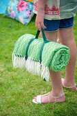 Rolled, green picnic blanket held by girl in garden