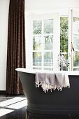 Cloth hanging over edge of free-standing vintage bathtub in front of half-open balcony door