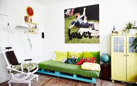 DIY sofa on blue-painted pallets, white-painted chair and yellow retro cabinet