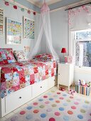 Colourful polka-dot rug next to bed with storage drawers and patchwork blanket in child's bedroom painted pale blue