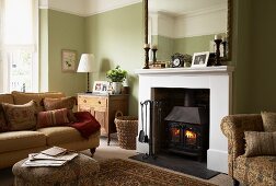 Gemütliches, traditionelles Wohnzimmer mit hellgrün getönter Wand, Couch vor Kamin mit Feuer