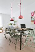 Black metal table, vintage folding chairs painted green and pendant lamps with pink lampshades in minimalist interior