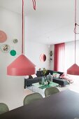 Pendant lamps with pink lampshades above dark dining table; grey corner sofa and retro coffee table in background