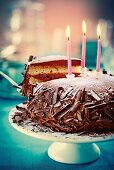 Chocolate cake with grated chocolate, icing sugar and candles on a cake stand