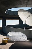 Designer outdoor sofa in white plastic with perforated pattern and Oriental parasol on sunny concrete ramp