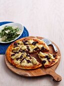 Pizza with artichokes and onion relish on a pizza board, served with rocket salad with parmesan cheese