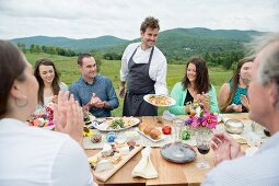 Family celebration outside; a young chef serving appetisers against a backdrop of green hills