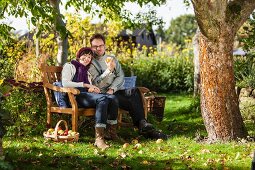 Frau und Mann auf Gartenbank in sonnenbeschienenem Garten bei der Apfelernte