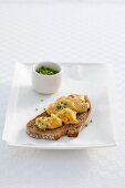 A slice of bread topped with scrambled eggs and chives