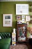 Grünes Chesterfield-Sofa im Anschnitt vor grüner Wand mit Bildern und antiker Vitrine