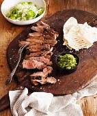 Gegrilltes Lamm in Scheiben mit Minz-Mandelpaste und Brot auf einem Holzbrett, dazu Fenchel-Gurkensalat