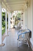 White rattan chair against wall of cottage veranda with white wooden structure
