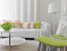 White couch with pastel scatter cushions, fruit bowl on coffee table and chair with matching foot stool