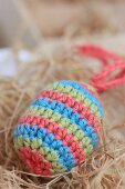 Striped, crocheted Easter egg amongst hay