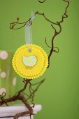 Hand-crafted, yellow felt rosette with Easter motif hanging from branch