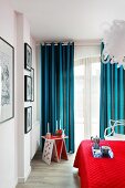 Candles on whimsical side table, blue and black striped curtains and red bedspread in comfortable bedroom