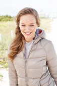 A young blonde woman outside wearing a beige quilted jacket