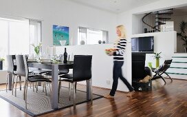 Black chairs around festively set table and woman in front of half-height wall in open-plan, modern interior