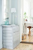 White table lamp on chest of drawers with pale varnish in corner of room next to open doorway