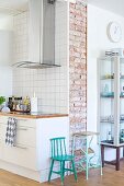 Retro child's chair and step stool painted turquoise between modern kitchen counter with stainless steel extractor hood and glass display cabinet