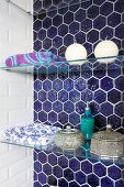 Bathing utensils and Moroccan caskets on glass shelves in niche with blue honeycomb tiles