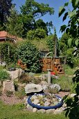 Blaue Pflanzschale mit Steinen und Sukkulenten arrangiert mit verschiedenen Kunstobjekten in sommerlichem Garten