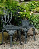 Ornate, antique, metal garden chairs and pink geranium in square pot with embossed pattern