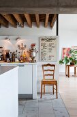 Kitchen chair next to white kitchen counter below rustic, wood-beamed ceiling in renovated loft apartment