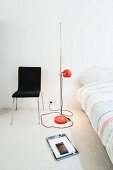 Retro standard lamp with red, spherical lampshade between black chair and bed