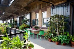 Lush greenery on urban balcony with various planters and seating area against loft-apartment façade