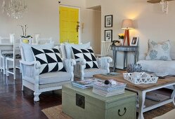 Vintage-style seating area with graphic-patterned scatter cushions on wicker armchairs, coffee table and old wooden trunk in front of yellow door