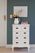 Jug of roses on white, country-house-style chest of drawers below picture on grey-painted wall