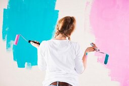 Junge Frau mit Farbrollen zwei verschiedene Wandfarben betrachtend