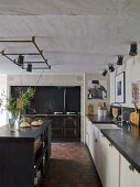 Kitchen counter with white base units and free-standing island counters on tiled floor in rustic interior