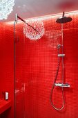 Rainfall shower and hand-held shower head on red tiled wall with reflection of pendant lamp