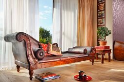 Elegante, antike Chaiselongue vor Panoramafenster mit luftigem Vorhang in traditionellem Ambiente