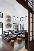 View through open Shoji sliding doors of charcoal sofa combination, black and white graphic artwork and windows with view of garden