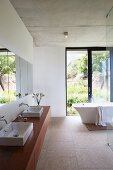 Waschtisch mit zwei Aufsaztbecken auf Holzunterbau, im Hintergrund freistehende Badewanne vor Terrassentür in minimalistischem Bad