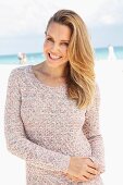 A blonde woman on a beach wearing a long, knitted jumper