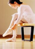 A girl wearing a white tutu putting on ballet shoes