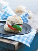 A bread roll with fresh cheese, tomato and basil leaves