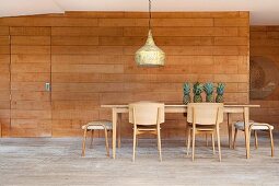 Pale wooden chairs, stools and table, fresh pineapples and vintage pendant lamp