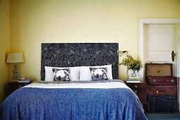 Vintage suitcases stacked against country-house interior door and bed with floral headboard in bedroom