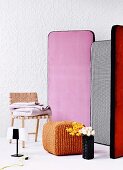 Bunte Stellwand, davor ein Stuhl mit Gurtbespannung, Flechthocker und Blumenvase