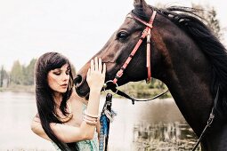 A young, dark-haired woman wearing a spaghetti strap top stroking a horse