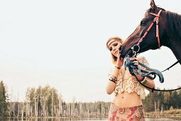 Junge blonde Frau im Hippie-Stil streichelt Pferd an See