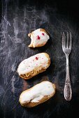 Mini eclairs, whole and half-eaten, on a dark metal surface